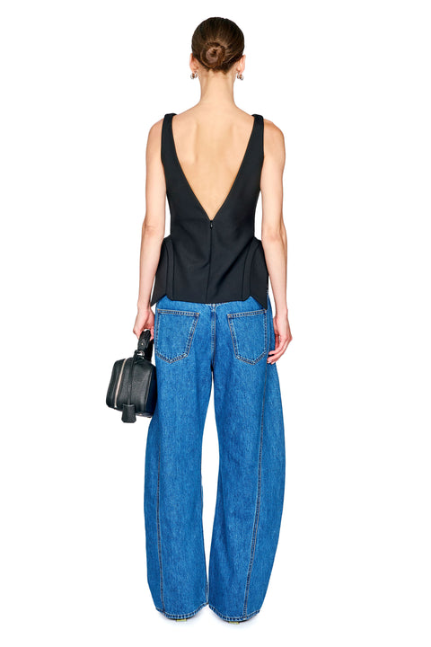 A woman shown from the back wearing a black sleeveless top with a deep V-back and wide-leg blue jeans, holding a small black handbag against a plain white background.