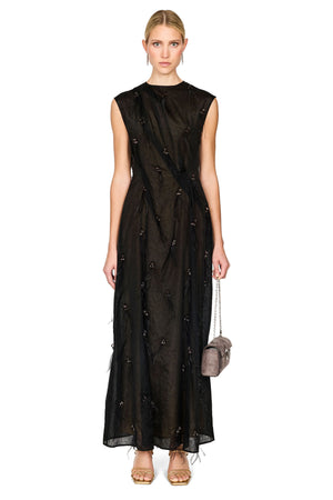 A model wearing a sleeveless black maxi dress with a sheer overlay and embroidered details, holding a small gray handbag against a plain white background.