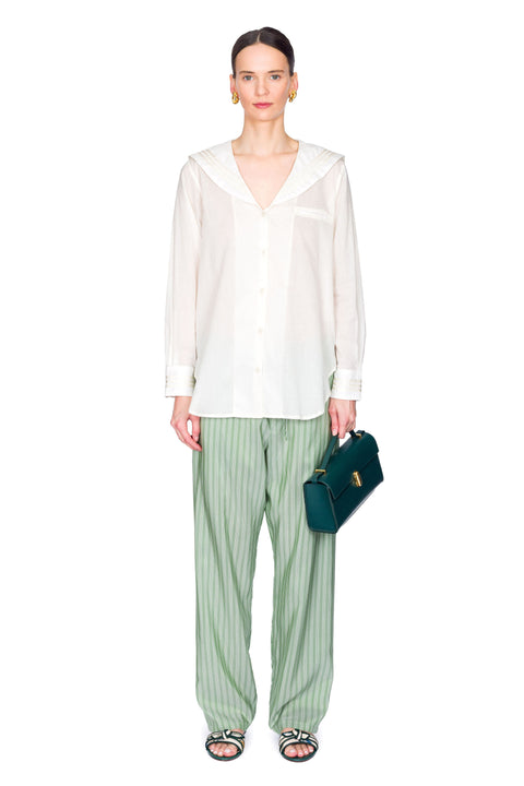 Centered view of woman wearing a white blouse and green striped pants holding a blue handbag on a white background