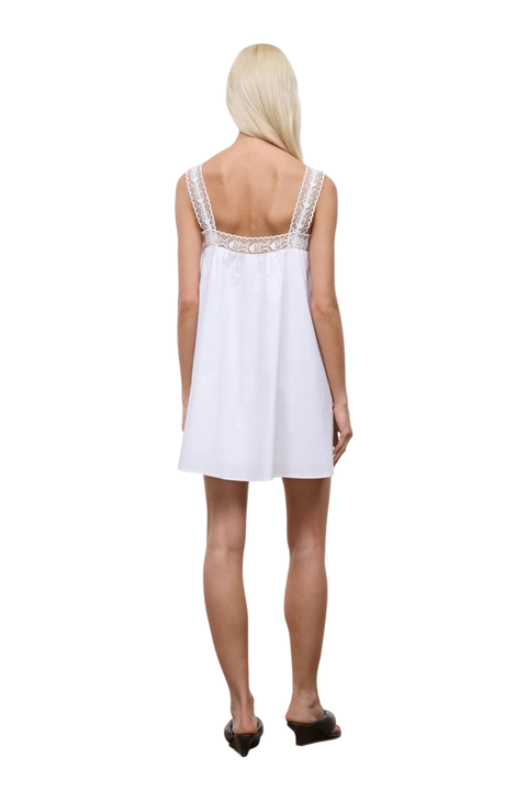 Woman wearing a white flowy mini dress with a lace trim on a white background back angle