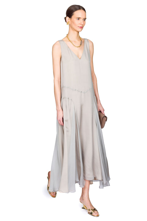 Woman wearing a light gray sleeveless dress and gold jewelry on a white background