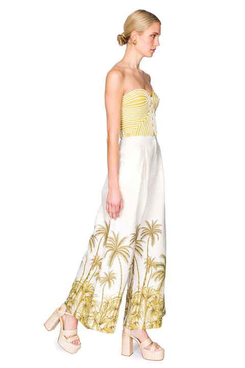 Side view of strapless green bustier top with white piping and white linen palazzo pants with palm tree patterning
