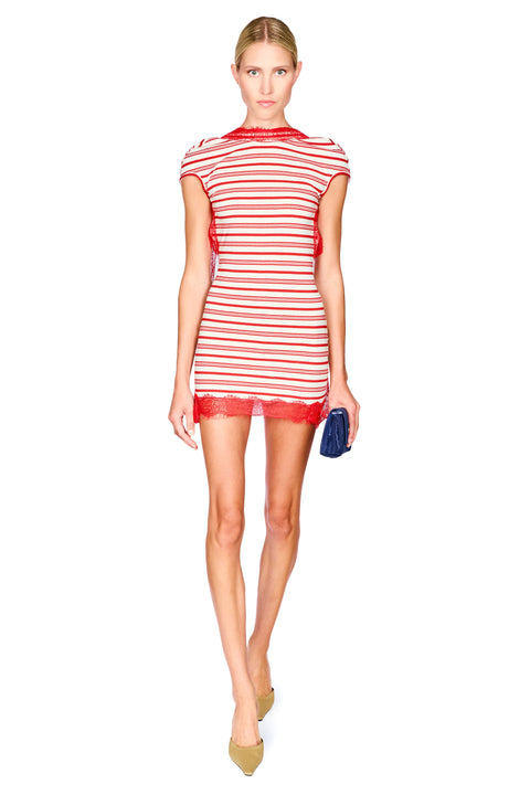 A woman modeling a red and white horizontally striped mini dress with red lace trim at the neckline and hem, holding a dark blue clutch, on a solid white background.