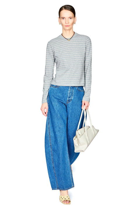 A woman modeling a gray and white striped long-sleeve knit top with wide-leg blue jeans, holding a light beige tote bag against a plain white background.