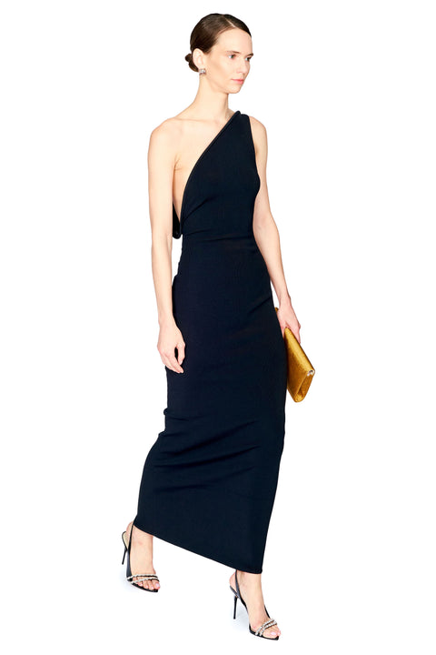 A woman modeling a black one-shoulder maxi dress with a draped neckline and side cutout, paired with high-heeled sandals and holding a gold clutch, against a plain white background.