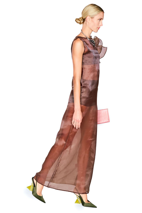 A woman modeling a sheer, floor-length brown dress with a ruffled shoulder detail, paired with olive green pointed heels and a small pink clutch, set against a plain white background.