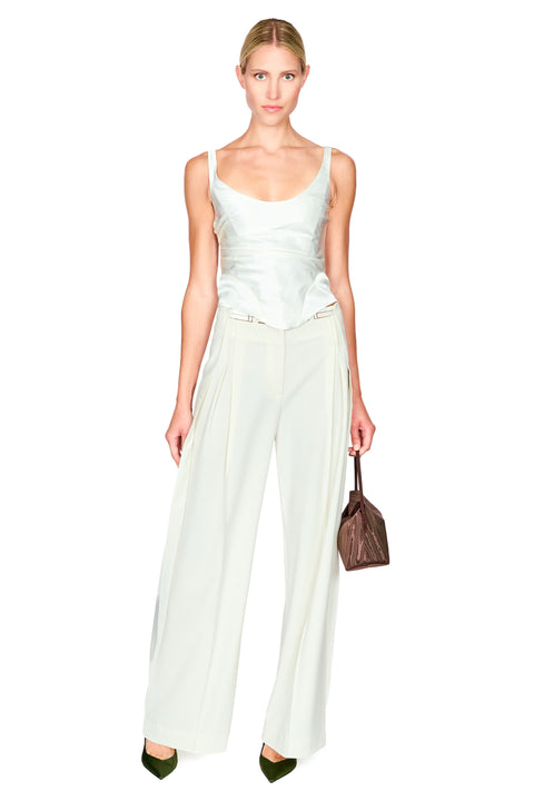 A woman modeling a white satin camisole top paired with matching wide-leg trousers, holding a brown textured handbag against a plain white background.