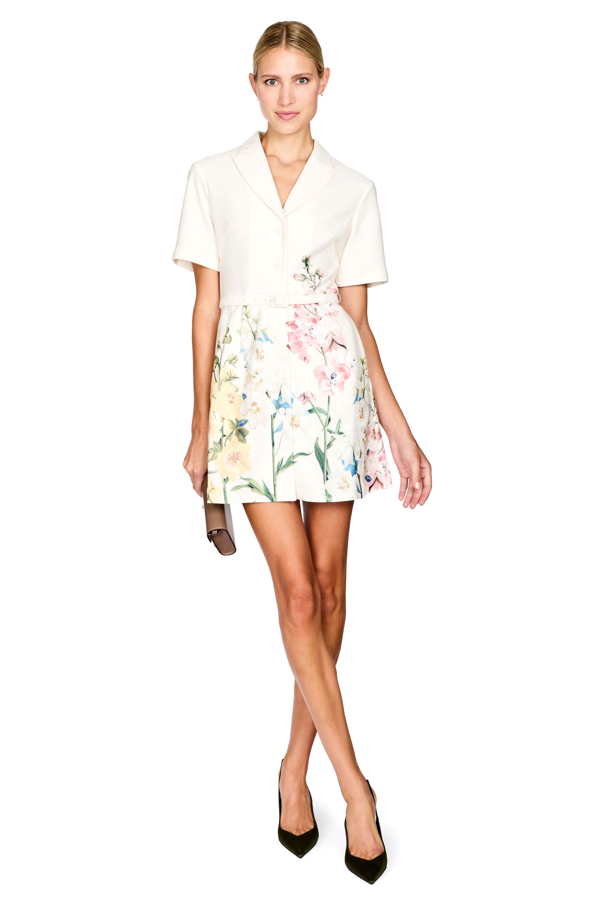 A woman modeling a short-sleeve collared white mini dress featuring a colorful floral print, holding a small brown clutch against a plain white background.