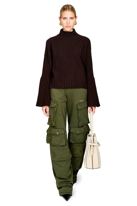 A model wearing a dark brown ribbed mock-neck long-sleeve top, olive green cargo pants, and holding a cream-colored leather handbag against a solid white background.
