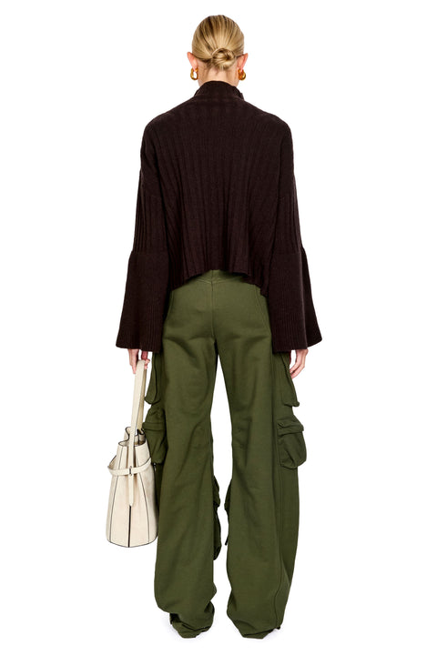 A model shown from the back wearing a dark brown ribbed long-sleeve cropped jacket and olive green wide-leg cargo pants, holding a cream-colored handbag against a solid white background.