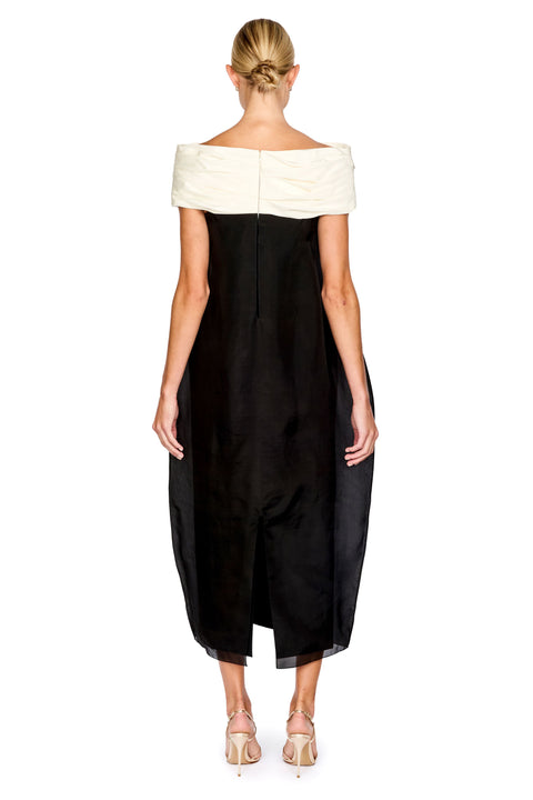 A woman shown from the back wearing a black off-the-shoulder midi dress with a contrasting cream off-the-shoulder yoke, paired with beige high-heeled sandals, against a plain white background.