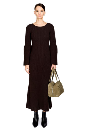 A model stands against a white background wearing a dark brown ribbed knit midi dress with long sleeves and holding an olive green suede shoulder bag.