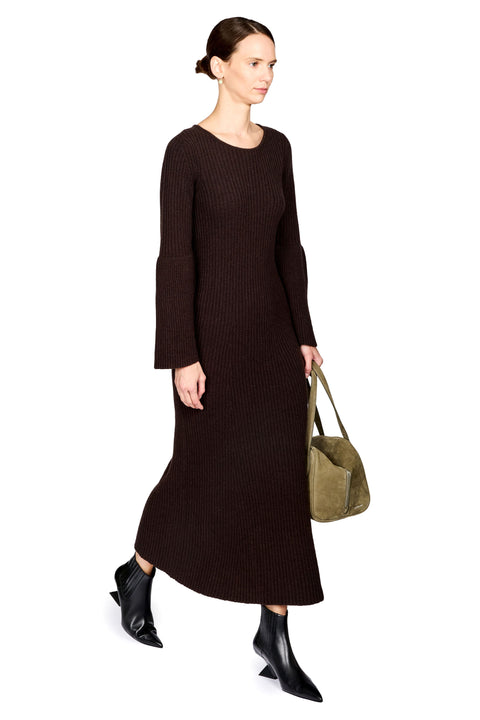 A woman modeling a dark brown ribbed knit midi dress with long sleeves, paired with black pointed ankle boots and holding an olive green tote bag, set against a plain white background.
