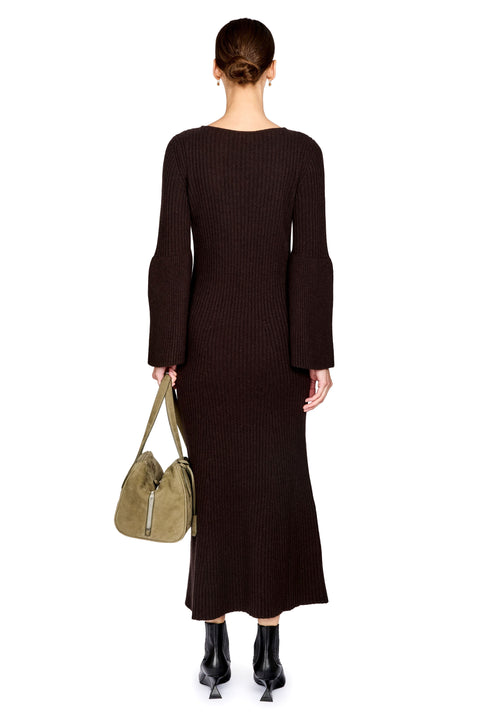A model shown from the back wearing a dark brown ribbed knit long-sleeve midi dress, holding an olive green handbag, and wearing black ankle boots against a white background.