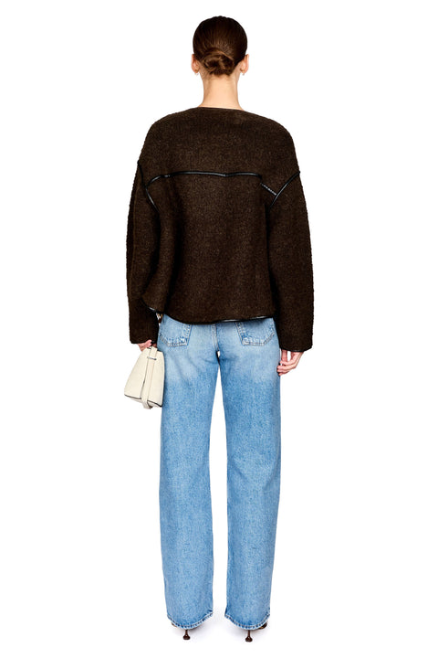 A model shown from the back wearing a dark brown textured knit sweater and light blue wide-leg jeans, holding a small white handbag against a plain white background.