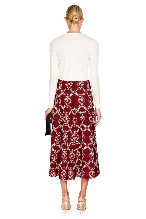 A woman shown from the back wearing a white long-sleeve top and a burgundy midi skirt with a cream geometric pattern, paired with beige high-heeled sandals against a plain white background.