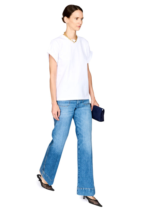 A woman modeling a white short-sleeve t-shirt and light-wash blue flare jeans, holding a small navy blue clutch purse, against a solid white background.