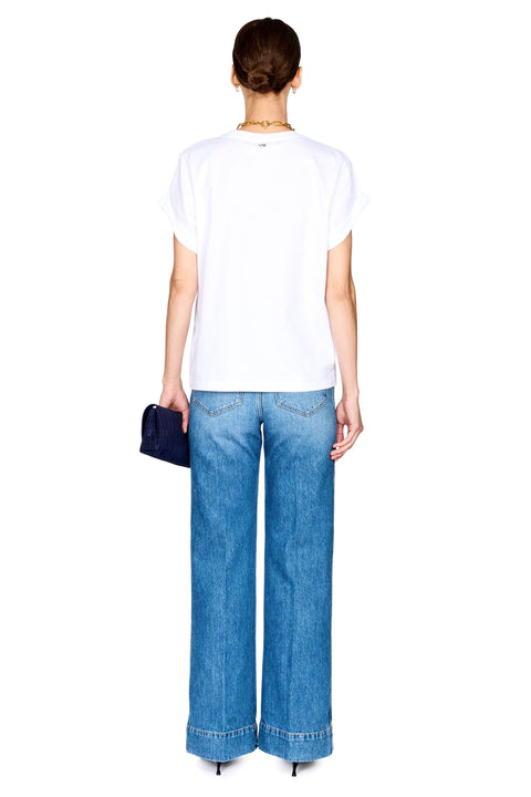 A woman shown from the back wearing a white short-sleeve t-shirt and wide-leg blue jeans, holding a small dark blue clutch against a plain white background.
