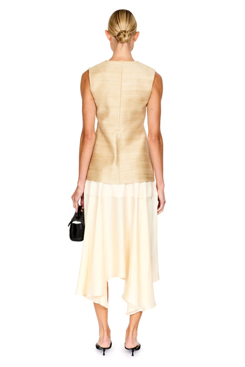 A woman shown from the back wearing a sleeveless textured beige top and a cream asymmetrical skirt, holding a small black handbag against a plain white background.