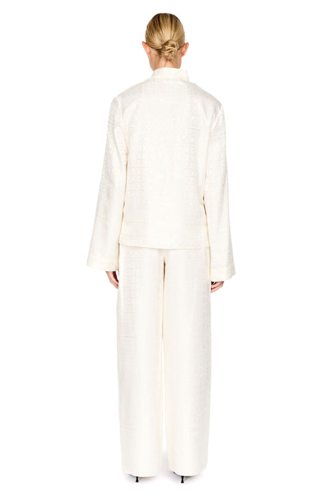 A model viewed from the back wearing a matching cream-colored textured jacket and wide-leg trousers set against a solid white background.