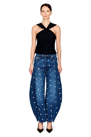 A model stands against a white background wearing a black halter-neck top and blue wide-leg jeans with a white floral pattern.