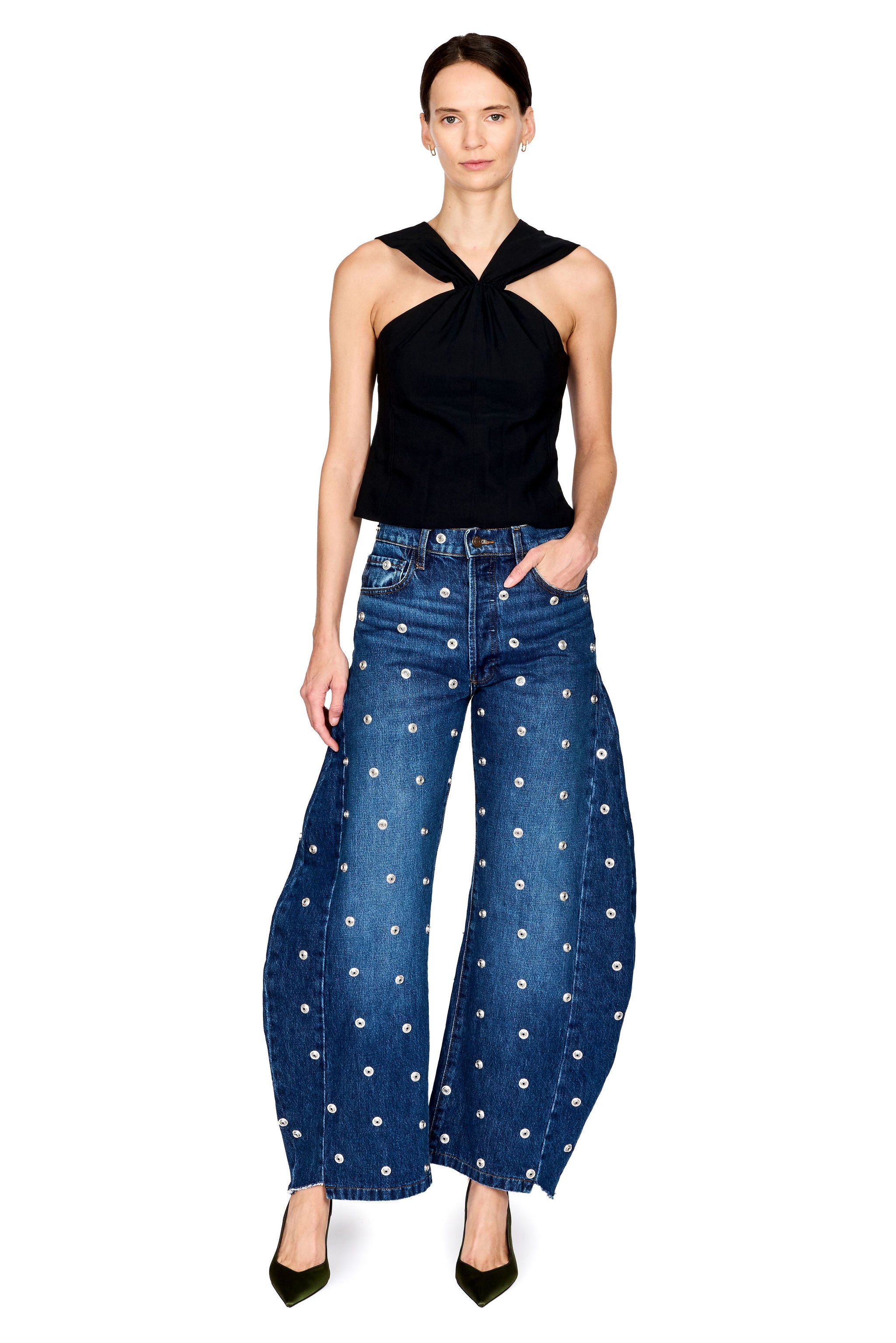 A model wearing a black halter top and blue wide-leg denim jeans with white embroidered dots, standing against a plain white background.