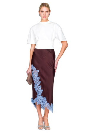 Woman wearing a white top and brown skirt with blue lace details on a white background