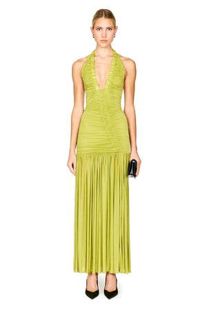A model wearing a sleeveless, halter-neck, floor-length lime green dress with ruching on the bodice and a pleated skirt, paired with black heels and holding a small black clutch, set against a plain white background.