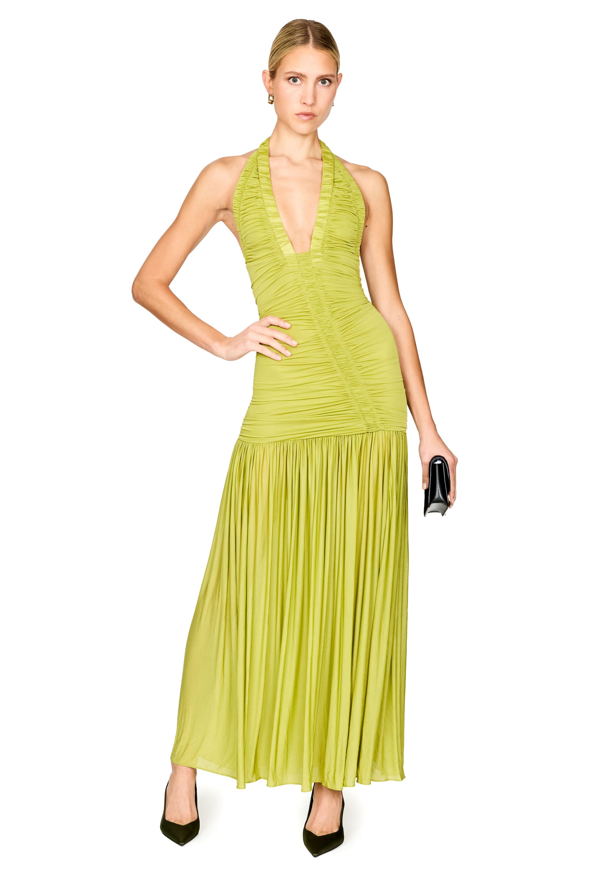 A woman modeling a sleeveless halter-neck maxi dress in a bright lime green color, featuring a ruched bodice and a pleated skirt, paired with black heels against a plain white background.