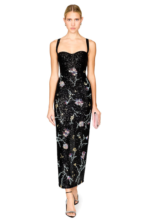 A model wearing a black spaghetti-strap midi dress covered in shimmering sequins and decorated with delicate floral patterns, paired with black strappy heels against a plain white background.