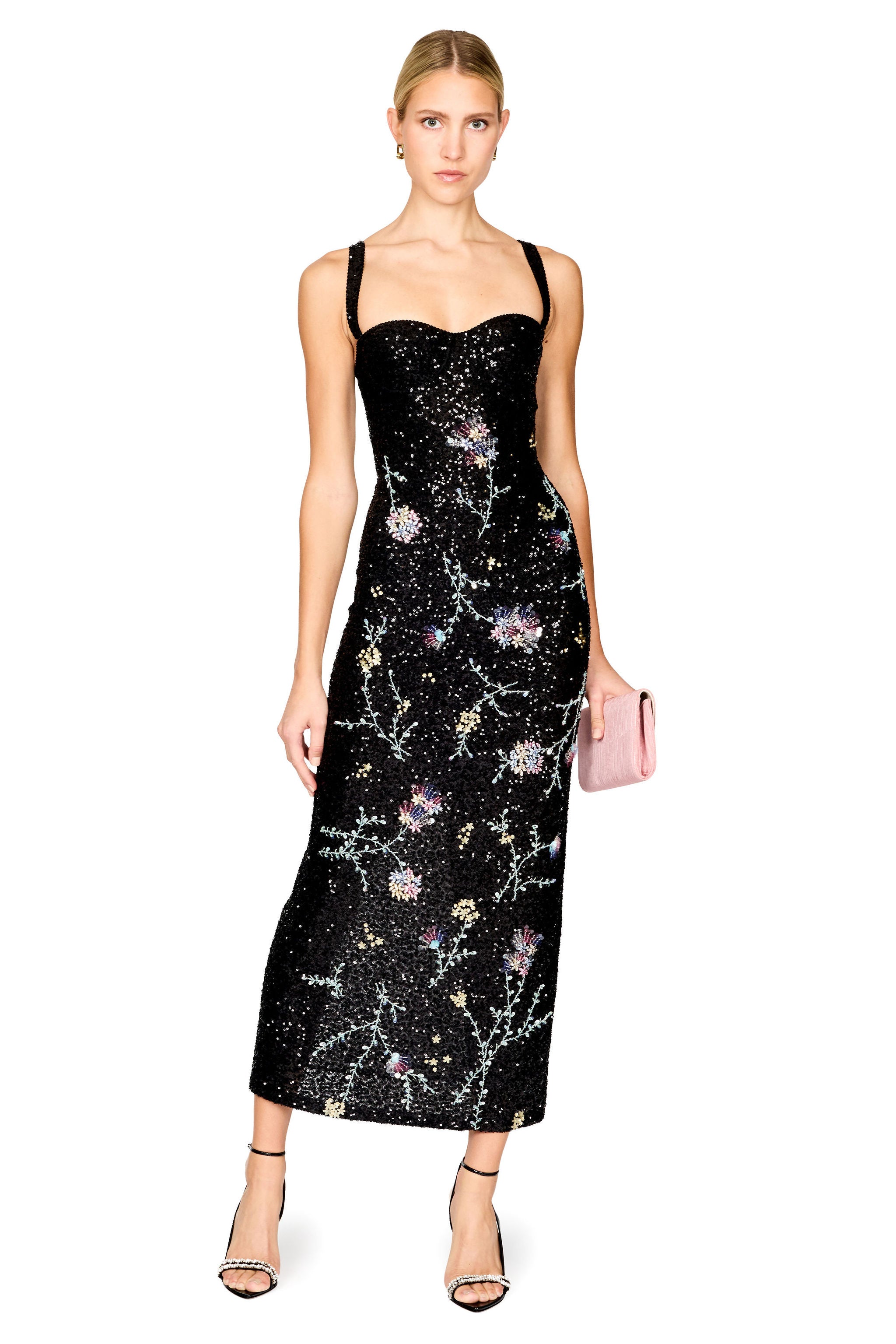 A model wearing a black sequined midi dress with a floral branch pattern in pastel colors, holding a pink clutch bag against a solid white background.