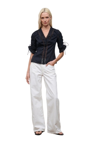 A woman wearing a black button-up top with cinched sleeves and lace detailing