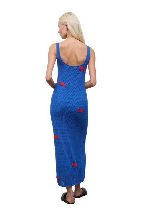 Woman wearing a blue crochet dress with red fish embroidery patterns on a white background back angle