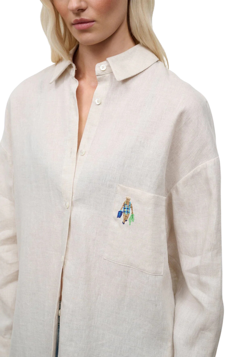 Close-up of a woman wearing a beige oversized linen button down with pocket embroidery