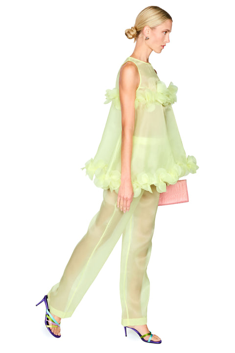 A woman modeling a sheer pale yellow-green sleeveless top with layered ruffle details and matching sheer wide-leg pants, shown in profile against a plain white background.